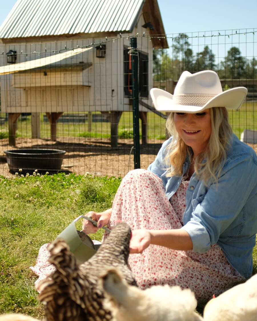 Sarah kneeling in the grass, feeding one of the hens